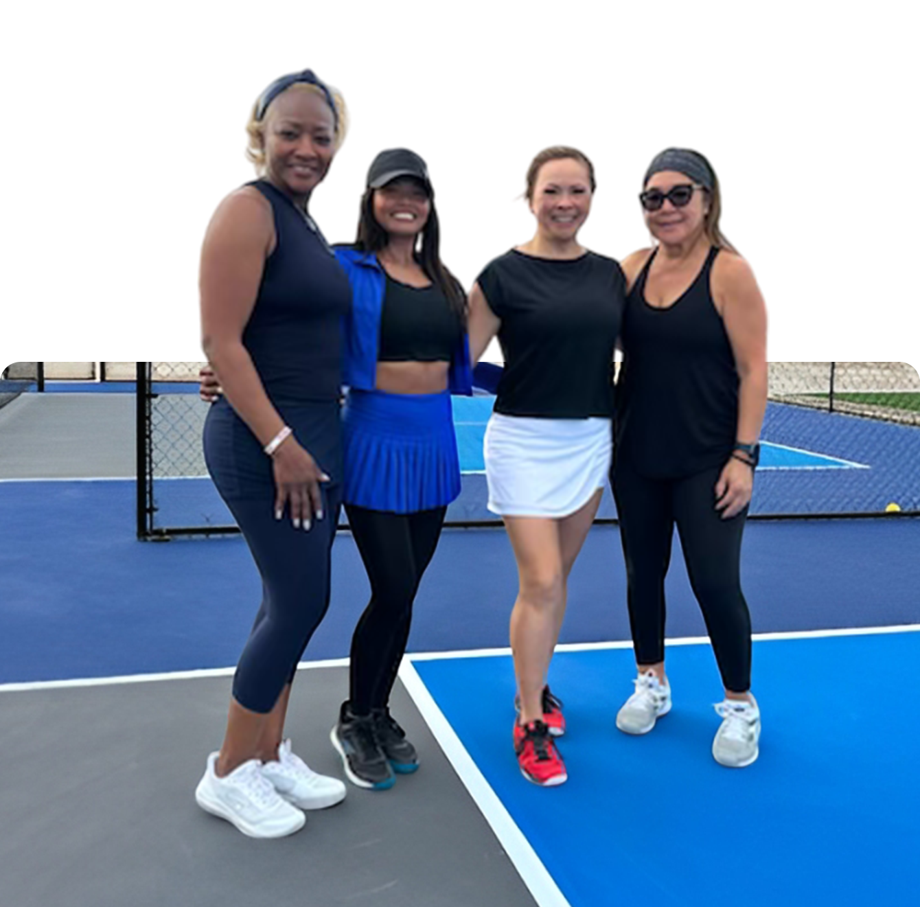 Four women standing on a tennis court holding rackets.